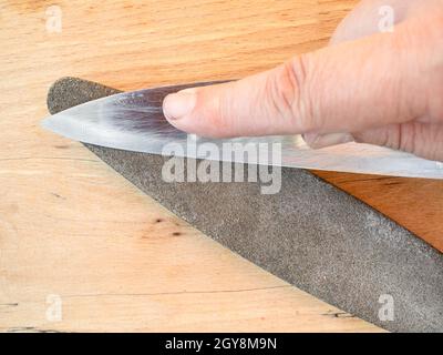 sharpening steel knife close up on whetstone on wooden board Stock Photo