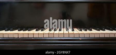 Old black grand piano keyboard with keys from ivory and ebony, part of a musical instrument in panoramic format, copy space, selected focus, narrow de Stock Photo