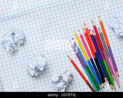 multicolored wooden pencils and crumpled sheets of paper on white squared paper background, top view Stock Photo