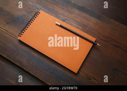 Orange notepad and pencil on wooden background. Blank stationery template. Stock Photo