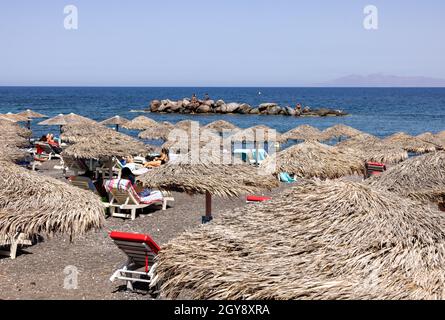 Kamari, Santorini, Greece - June 27, 2021: Sun loungers on the black volcanic beach of Kamari in Santorini. Cyclades, Greece Stock Photo