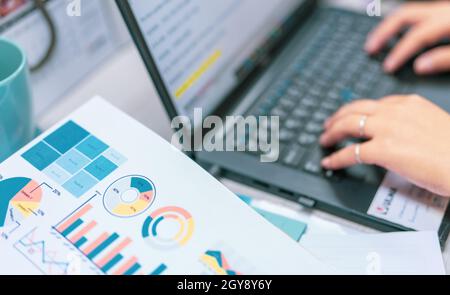 Sale report and business financial graph chart on blur office worker hand typing on the laptop at the computer desk. Paperwork from an accountant. Doc Stock Photo