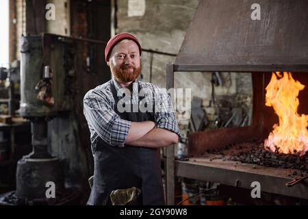 Portrait of mature bearded carpenter standing with arms crossed and looking at camera working in the workshop Stock Photo