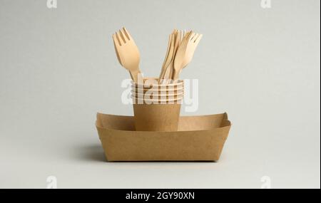 disposable brown paper cups, rectangular plates and wooden forks on a gray background. Zero waste, no plastic Stock Photo