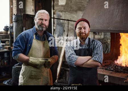 Portrait of two carpenters in aprons looking at camera while working in the workshop Stock Photo