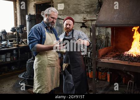 Two manual workers using digital tablet in their work while working in team at the factory Stock Photo