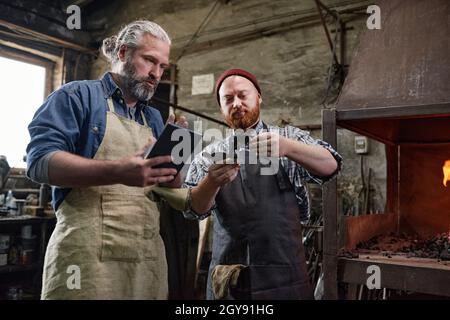 Man showing the metallic detail to his colleague while he using tablet pc they working in team in the factory Stock Photo