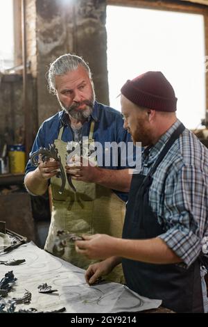 Man holding metallic detail in his hands and showing to his colleague the process of creation Stock Photo