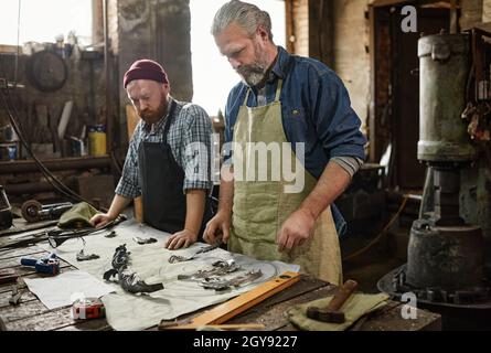 Two colleagues standing near the table with tools and making details together in the workshop Stock Photo