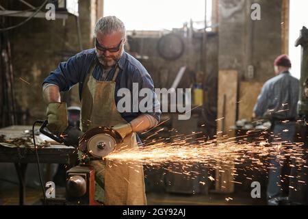 Manual worker using grinder to cut metallic detail in the workshop Stock Photo