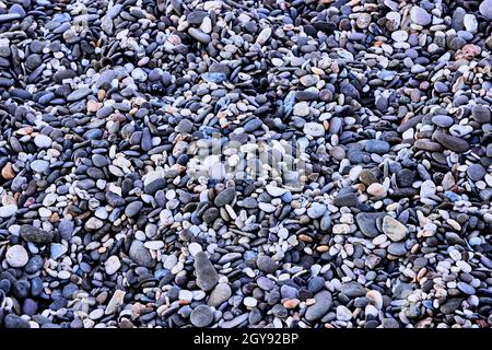 Background of small sea pebbles, top view. The texture of sea stones. Stones on the sea. Natural materials and colors of sea stones. Purple-blue. Stock Photo