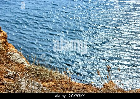 Natural abstract background. View of the calm blue sea from the cliff. Ripples on the water surface. Selective focus on a small piece of rock. Stock Photo