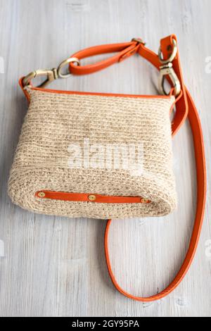 bottom view of hand-knitted casual cross body bag with orange leather belt on gray wooden table Stock Photo