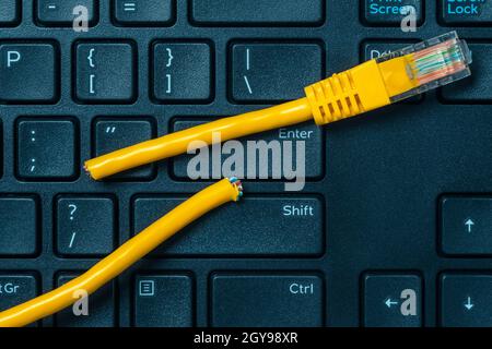 Internet connection disconnected. Computer keyboard with yellow network cable cutted off Stock Photo