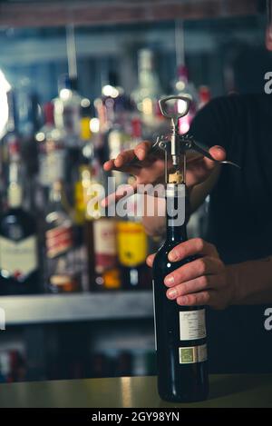 waiter opening a bottle of wine using a wine opener, on the bar counter, bottom of bottles inside the bar Stock Photo