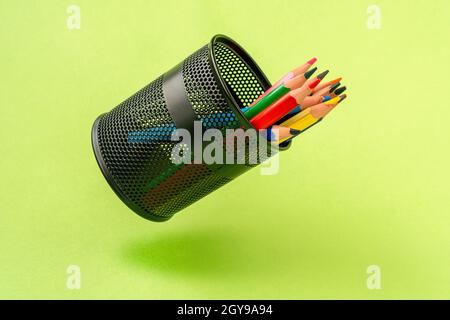 Colored pencils in a black mesh pen pot on a green background Stock Photo