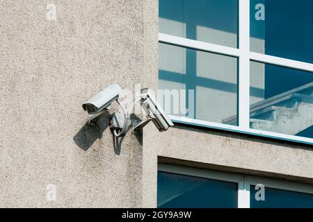 Two CCTV cameras on grey building wall with big windows Stock Photo