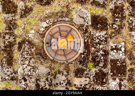 Old round iron manhole on the abandoned old tile with grass growing between the joints of the tile Stock Photo