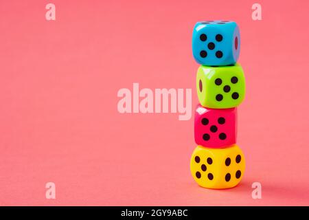 Stack of colorful dice on pink background. Copy space. Stock Photo