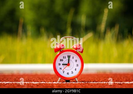 Red alarm clock on to the running track in the stadium. Stock Photo