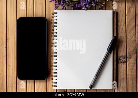 Empty Open Journal Beside Mobile With Pens On Top Of Wooden Desk. Stock Photo