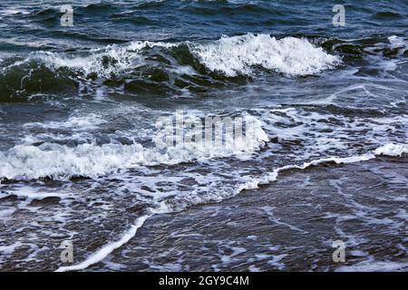 Strong waves with bright white sea foam. The raging sea in bad weather. Dark sea or ocean. An incoming wave. Storm waves at sea. Stock Photo