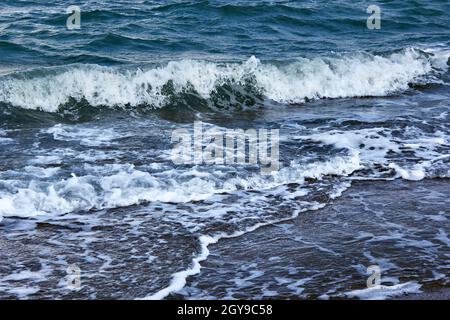 Strong waves with bright white sea foam. The raging blue sea in bad weather. Dark sea or ocean. An incoming wave. Storm waves at sea. Stock Photo