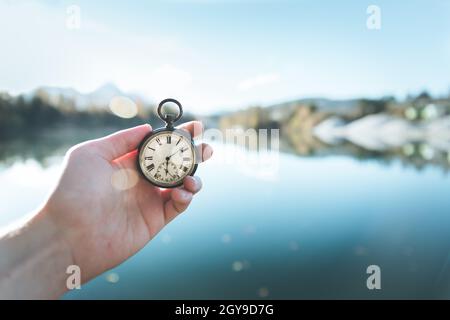 Hand held stop watch outdoors, autumn, blurry blue lake in the background Stock Photo