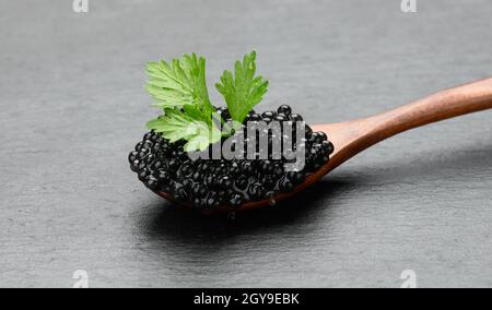 fresh grainy black paddlefish caviar in brown wooden spoon on a black background, close up Stock Photo