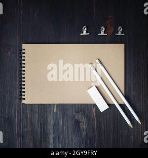 Photo of closed blank kraft sketchbook, pencils and eraser on wood table background. Template for placing your design. Flat lay. Stock Photo