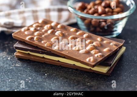 Various chocolate bars with hazelnuts on black table. Stock Photo