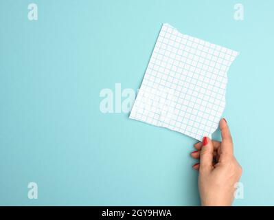 female hand holding a torn blank sheet of paper in a cage on a blue background Stock Photo