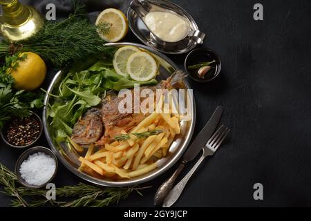 Fried fish dorado with potatoes chips, fresh herbs and lemon Stock Photo