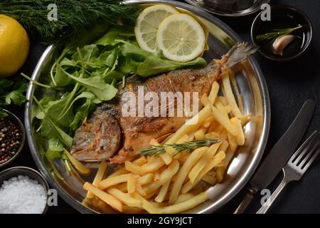 Fried fish dorado with potatoes chips, fresh herbs and lemon Stock Photo