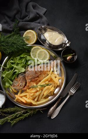 Fried fish dorado with potatoes chips, fresh herbs and lemon Stock Photo