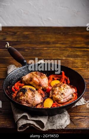 Chicken thighs baked with red bell peppers, rosemary and lemon in cast iron skillet. Stock Photo