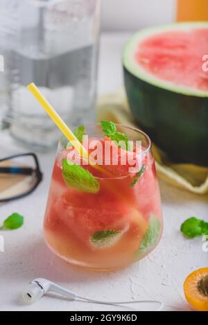Fresh watermelon cocktail with gin and soda, garnished with mint leaves and yellow straw in glass on light concrete background. Stock Photo
