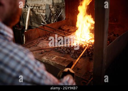 Close-up of blacksmiths holding metallic sticks and heating them with fire in the furnace Stock Photo
