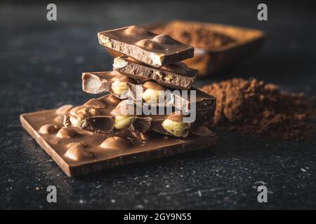 Nutty chocolate with hazelnuts and cocoa powder on black table. Stock Photo