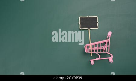 pink miniature shopping cart on green background. Seasonal sale, copy space Stock Photo