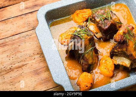 Beef ribs stewed in apricots. Veal meat with fruit sauce on rustic wooden background Stock Photo