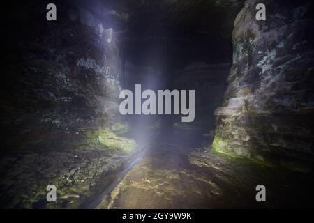 Shaft of light in a large cave with a tiny creek running through it Stock Photo