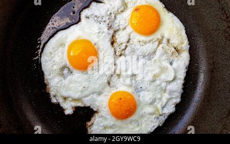Three free range fried eggs in a hot non stick frying pan. Stock Photo