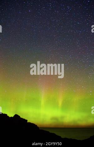 Starry night with wave of green aurora lights out over a large lake ocean or sea with coast silhouette Stock Photo
