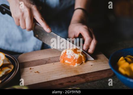 Closeup of hands and knife cutting orange on wooden cutting board Stock Photo