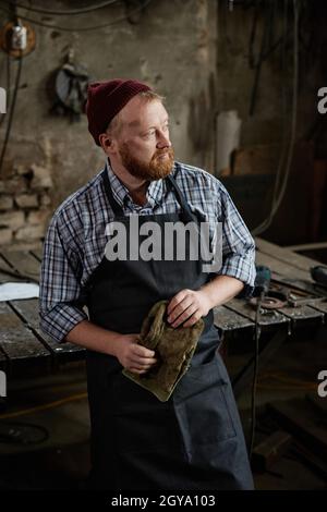 Portrait of mature manual worker in apron looking away standing in the workshop Stock Photo