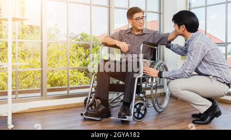 Asian senior disabled businessman in wheelchair discuss interacting together with the team in the office. The old man in a wheelchair and his young so Stock Photo