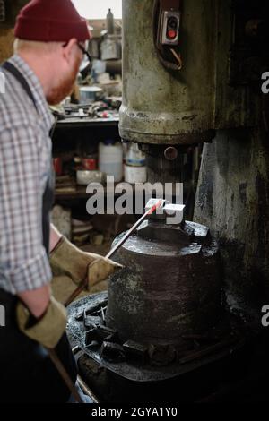 Rear view of blacksmith using tool to forge the detail from iron in the workshop Stock Photo