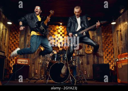 Two brutal musicians jumps with electric guitars, music performing on stage. Rock band performance or repetition in garage, man with musical instrumen Stock Photo