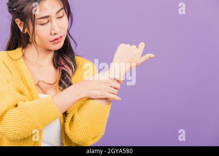Portrait of Asian beautiful young woman sad with wrist pain from carpal tunnel syndrome, female hand injury feeling pain, studio shot isolated on purp Stock Photo